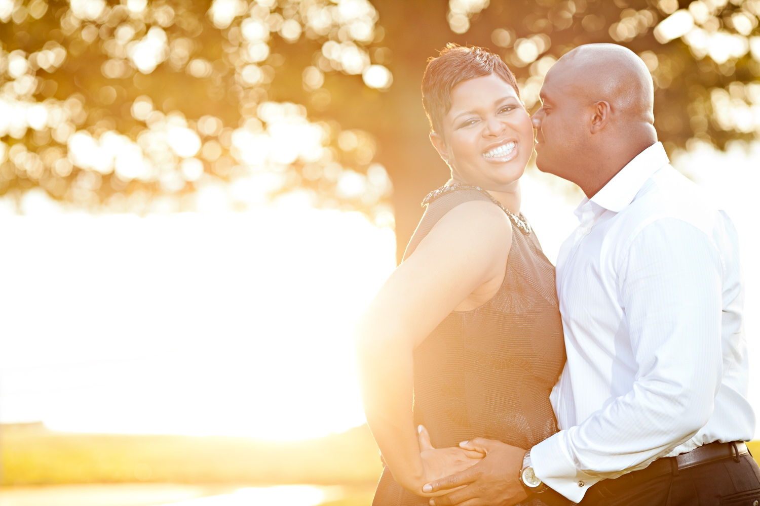 This engagement session was in Alexandria, Virginia, This black couple is nuzzling with the sun rising behind them, The warm glow of the sun is radiating throughout the photo, She is in a black dress and he is in a suit, Her smile is absolutely joyful, Procopio Photography, best top Washington DC photographer, best top Maryland photographer, best top Virginia photographer, best top DMV photographer, best top wedding photographer, best top commercial photographer, best top portrait photographer, best top boudoir photographer, modern fine art portraits, dramatic, unique, different, bold, editorial, photojournalism, award winning photographer, published photographer, memorable images, be different, stand out, engagement photography