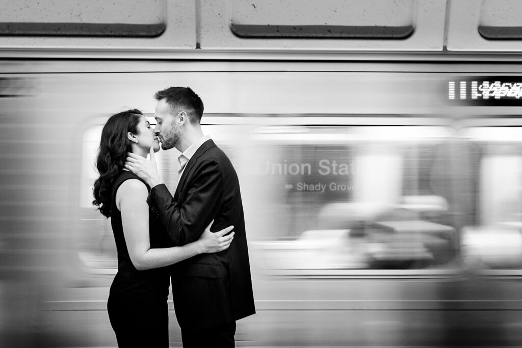 This photo was taken at the Union Station Metro Platform in Washington DC, the train is buzzing by in a blur of movement but you can still see the Union Station sign peeking through the blurred window of the moving metro car, the photo is in black and white, the gal is Indian, they are kissing in front of the train as it comes in, Procopio Photography, best top Washington DC photographer, best top Maryland photographer, best top Virginia photographer, best top DMV photographer, best top wedding photographer, best top commercial photographer, best top portrait photographer, best top boudoir photographer, modern fine art portraits, dramatic, unique, different, bold, editorial, photojournalism, award winning photographer, published photographer, memorable images, be different, stand out, engagement photography