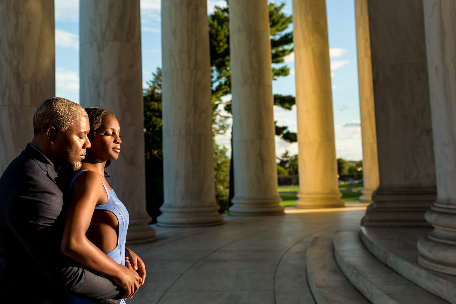 black couple at the Jefferson Memorial, cut out bright blue long dress, golden hour photos, the guy is behind the gal and they are cuddling while the setting sun is kissing their faces, they are inside the columns and the sun is glowing in the background, Procopio Photography, best top Washington DC photographer, best top Maryland photographer, best top Virginia photographer, best top DMV photographer, best top wedding photographer, best top commercial photographer, best top portrait photographer, best top boudoir photographer, modern fine art portraits, dramatic, unique, different, bold, editorial, photojournalism, award winning photographer, published photographer, memorable images, be different, stand out, engagement photography