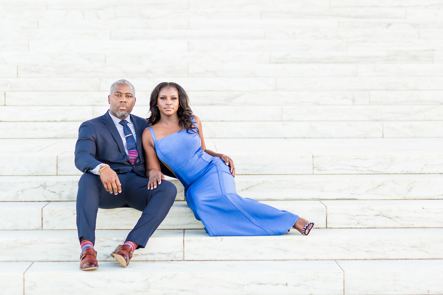 This photo was taken on the steps of the Jefferson memorial in Washington DC, Our goal is to create modern fine art portraits, This black couple is editorially posed, The guy is sitting and the gal is lounging with her long periwinkle dress, Her arm is on his leg and they look like a perfect pair, Procopio Photography, best top Washington DC photographer, best top Maryland photographer, best top Virginia photographer, best top DMV photographer, best top wedding photographer, best top commercial photographer, best top portrait photographer, best top boudoir photographer, modern fine art portraits, dramatic, unique, different, bold, editorial, photojournalism, award winning photographer, published photographer, memorable images, be different, stand out, engagement photography