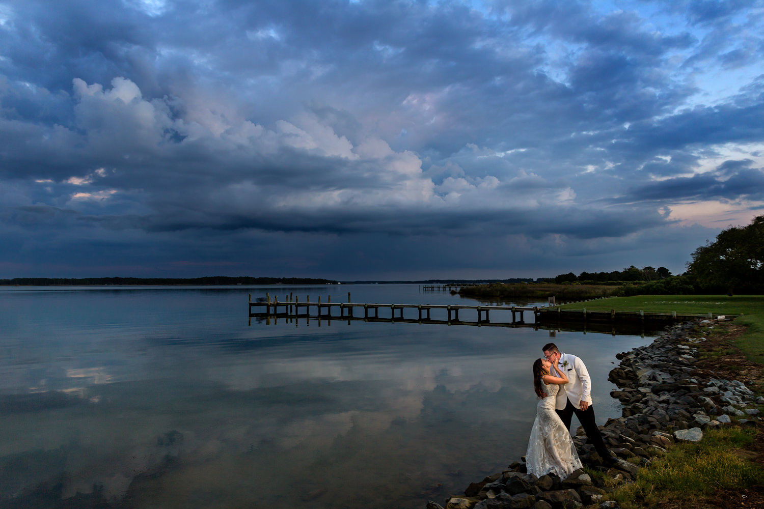 Swan Cove Manor, This eastern Shore wedding was lots of fun, the bride and groom came out from their reception to do a sunset shot with me, we caught the last bit of light as dusk was setting in, they were standing at the edge of the water and you can see the clouds and the reflection of the clouds in the water, it is dark blue in the sky and in the water, she reaches in to steal a kiss, they are standing on the rocks, Procopio Photography, best top Washington DC photographer, best top Maryland photographer, best top Virginia photographer, best top DMV photographer, best top wedding photographer, best top commercial photographer, best top portrait photographer, best top boudoir photographer, modern fine art portraits, dramatic, unique, different, bold, editorial, photojournalism, award winning photographer, published photographer, memorable images, be different, stand out