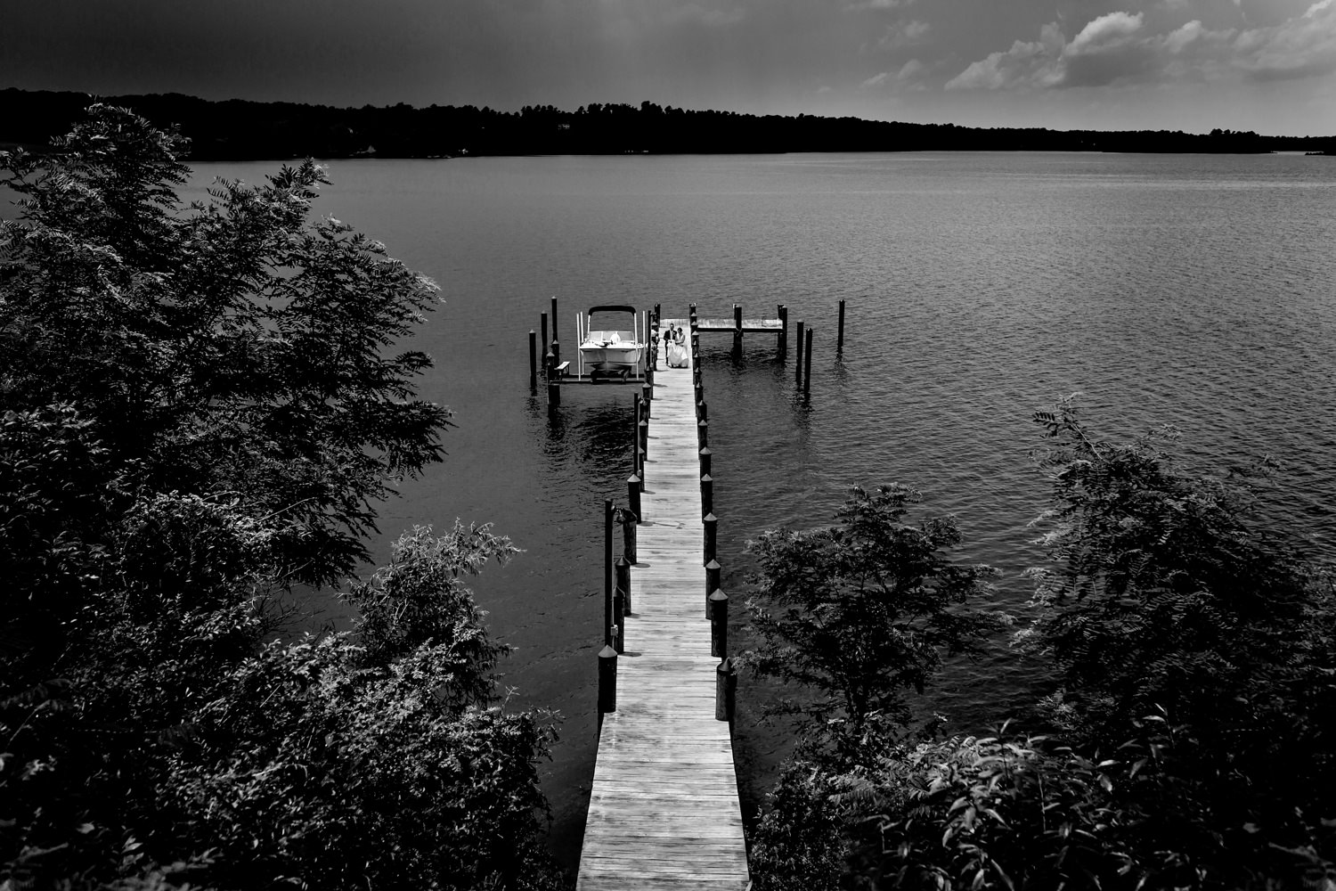 Eastern shore wedding, the bride and groom walked far out on a dock and started coming back, this black and white photo is a landscape of the water and the long dock stretching far out into the distance, the couple is small in the frame, Procopio Photography, best top Washington DC photographer, best top Maryland photographer, best top Virginia photographer, best top DMV photographer, best top wedding photographer, best top commercial photographer, best top portrait photographer, best top boudoir photographer, modern fine art portraits, dramatic, unique, different, bold, editorial, photojournalism, award winning photographer, published photographer, memorable images, be different, stand out