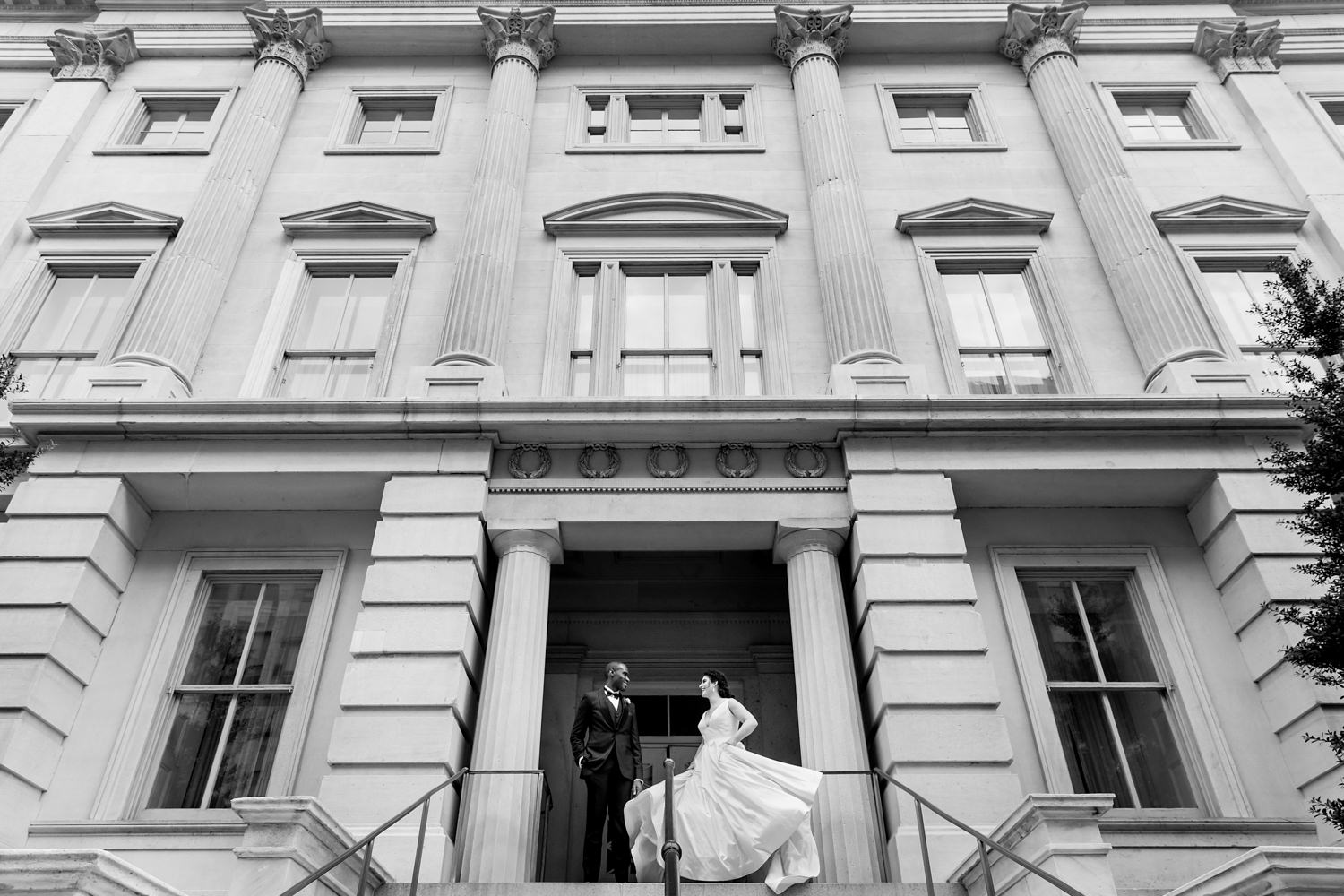 This wedding had bride and groom prep at the hotel Monaco in Chinatown, Washington DC, these are portraits just outside of the hotel, the ceremony and reception were at the Newseum, the bride is swishing her dress, the groom is admiring her and you can see the whole side of the building, this is a black and white photo, the groom is black and the bride is white, Procopio Photography, best top Washington DC photographer, best top Maryland photographer, best top Virginia photographer, best top DMV photographer, best top wedding photographer, best top commercial photographer, best top portrait photographer, best top boudoir photographer, modern fine art portraits, dramatic, unique, different, bold, editorial, photojournalism, award winning photographer, published photographer, memorable images, be different, stand out