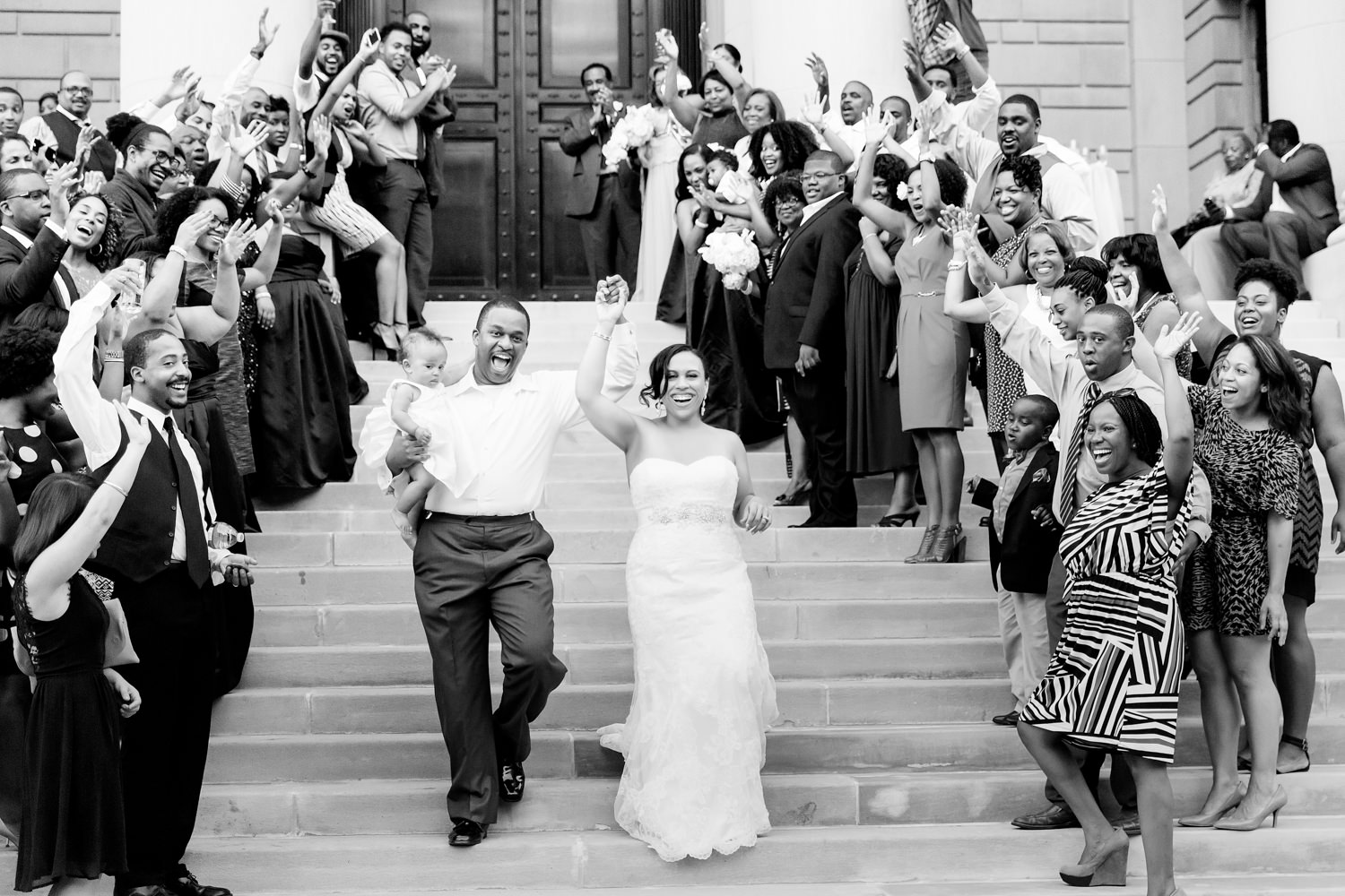 Carnegie Institution of Science in Washington DC, black bride and groom cheering as they exit the building, a crowd of people is on their left and right also cheering for them, the couple is walking down the steps all smiles, holding hands up in the air, and the groom is holding their baby, modern bride, Procopio Photography, best top Washington DC photographer, best top Maryland photographer, best top Virginia photographer, best top DMV photographer, best top wedding photographer, best top commercial photographer, best top portrait photographer, best top boudoir photographer, modern fine art portraits, dramatic, unique, different, bold, editorial, photojournalism, award winning photographer, published photographer, memorable images, be different, stand out