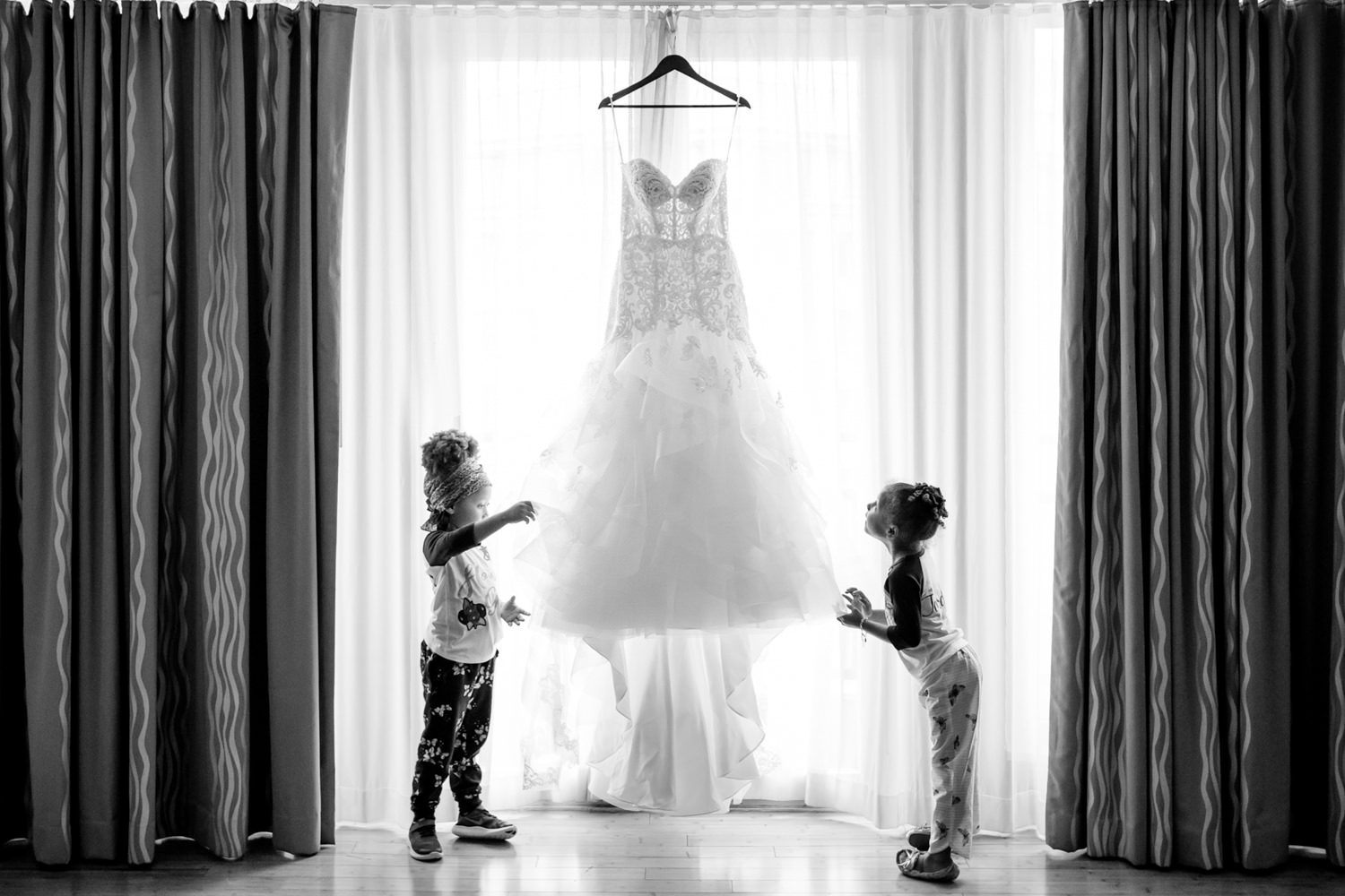These two adorable little girls are inspecting the wedding gown that is hung on the window, They stare in awe at the beauty of the dress, This is a black and white photo, Catching the moment, Procopio Photography, best top Washington DC photographer, best top Maryland photographer, best top Virginia photographer, best top DMV photographer, best top wedding photographer, best top commercial photographer, best top portrait photographer, best top boudoir photographer, modern fine art portraits, dramatic, unique, different, bold, editorial, photojournalism, award winning photographer, published photographer, memorable images, be different, stand out