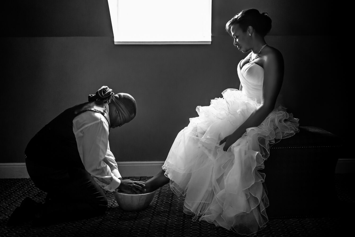 The groom did not want to see his bride prior to the ceremony hence why he was blindfolded, he did want to do a Biblical ritual and wash her feet, this is a dramatic black and white photo and you have profiles of the bride and groom, the bride is on a chair and the groom is on his knees washing her feet, black couple, Procopio Photography, best top Washington DC photographer, best top Maryland photographer, best top Virginia photographer, best top DMV photographer, best top wedding photographer, best top commercial photographer, best top portrait photographer, best top boudoir photographer, modern fine art portraits, dramatic, unique, different, bold, editorial, photojournalism, award winning photographer, published photographer, memorable images, be different, stand out