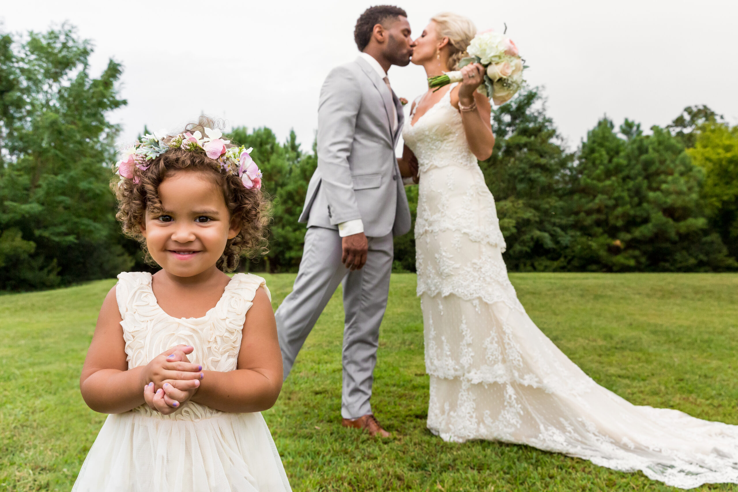 Procopio Photography, best top Washington DC photographer photography, best top Maryland photographer photography, best top Virginia photographer photography, best top DMV photographer photography, best top commercial photographer photography, best top wedding photographer photography, best top portrait photographer photography, best top boudoir photographer photography, modern fine art portraits, dramatic, unique, different, bold, editorial, photojournalism, award winning photographer, published photographer, memorable images, be different, stand out, luxe wedding, luxury wedding, luxury portraits, luxury boudoir, bespoke, waterfront wedding, black groom, white bride, bride and groom kissing in a field with the flower girl in front of them clearly photo bombing the portrait, her little hands are folded in front of her and she is smiling, knowing she is the focus of the photo and not the bride and groom, adorable flower girl with a flower crown